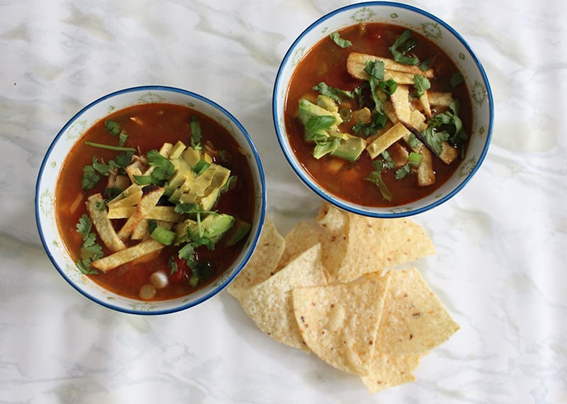 Two bowls with tortilla chips near them. In the bowls is the Shredded Chicken Tortilla Soup