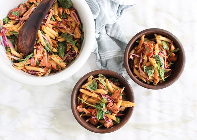 Tandoori Chicken Pasta Salad is in a large white bowl and two small brown bowls on a tabletop