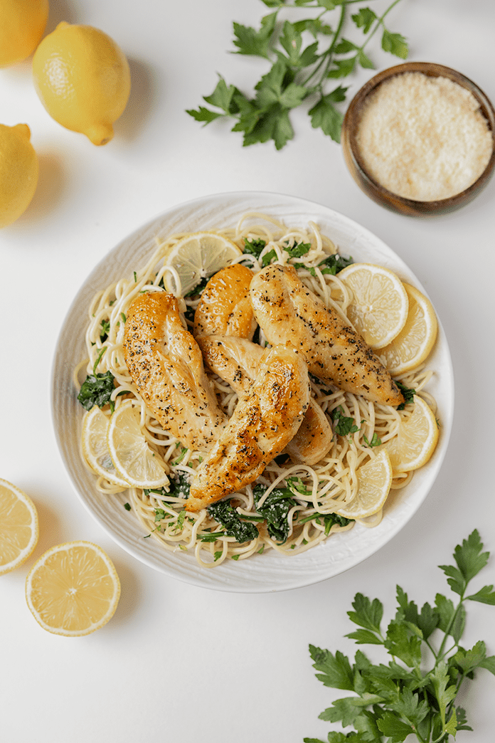 Lemon Butter Chicken Pasta on a plate surrounded by lemons and greens
